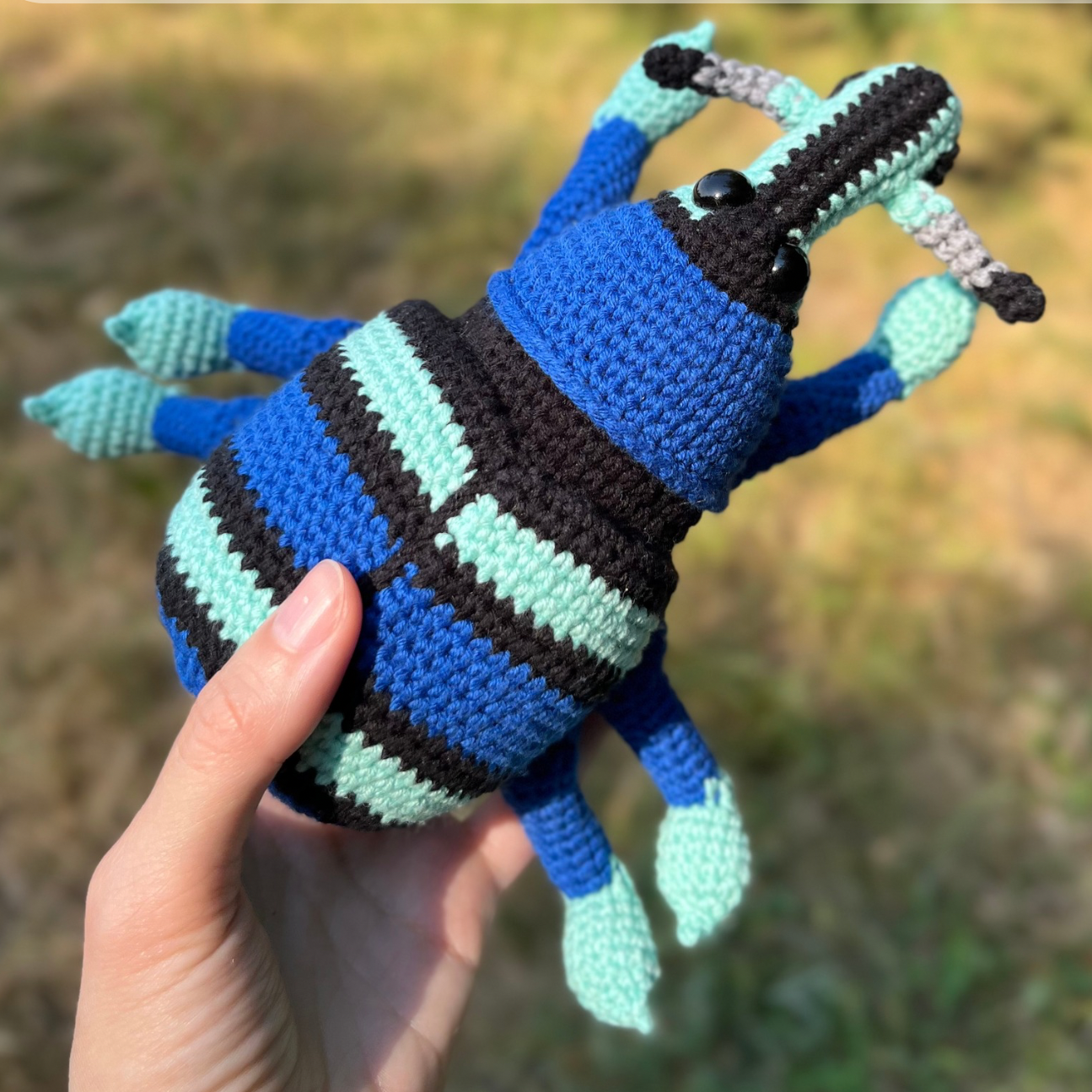 Handmade crocheted blue weevil in the hand