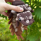 A hand holds a crochete hellgrammite a brown and cream patterned against a blurred green outdoor background.