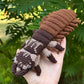 A crocheted hellgrammite toy held in a person's hand, with a lush green outdoor background of foliage.