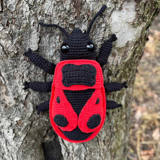 Hand-crocheted red and black red firebug, photographed against tree bar
