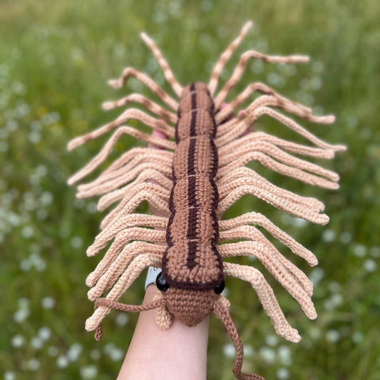 Crocheted centipede toy held by a person against a natural background